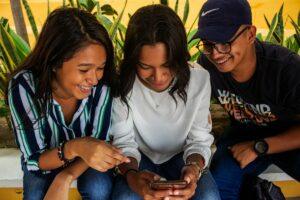 two women and a man smiling while looking at a phone