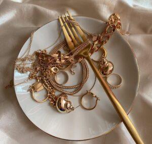 golden jewelry and golden fork on white saucer on beige silk